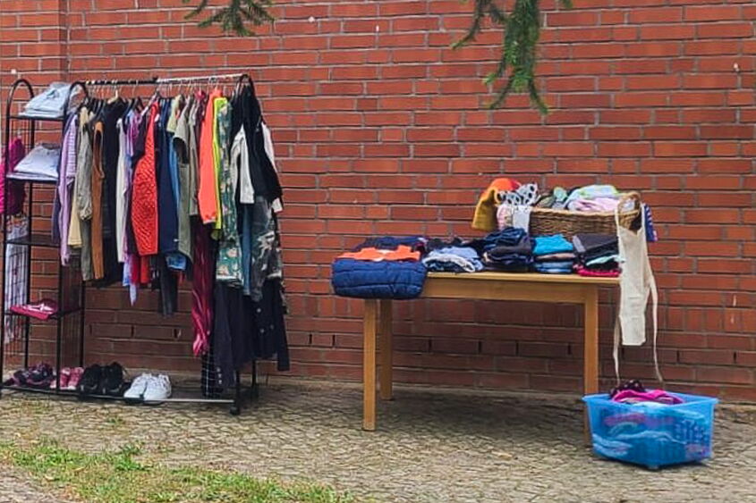 ein Kleiderständer link voll mit Kleidung und auch ein voller Tisch