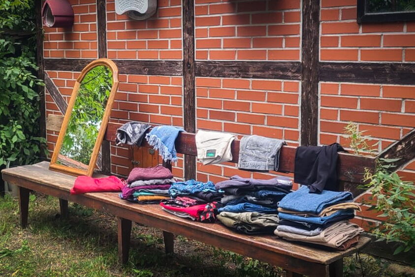 ein Spiegel steht auf einer Bank. Darauf liegen diverse Hosen