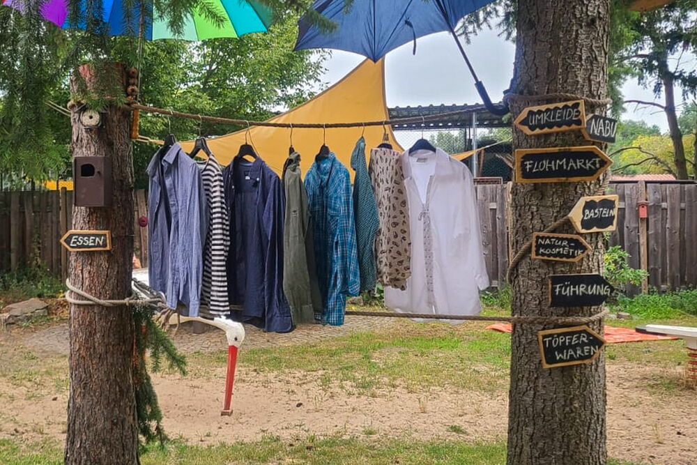 zwischen zwei Bäumen ist eine Wäscheleine gespannt, daran hängen Hemden, an den Bäumen sind Wegweiser zu erkennen