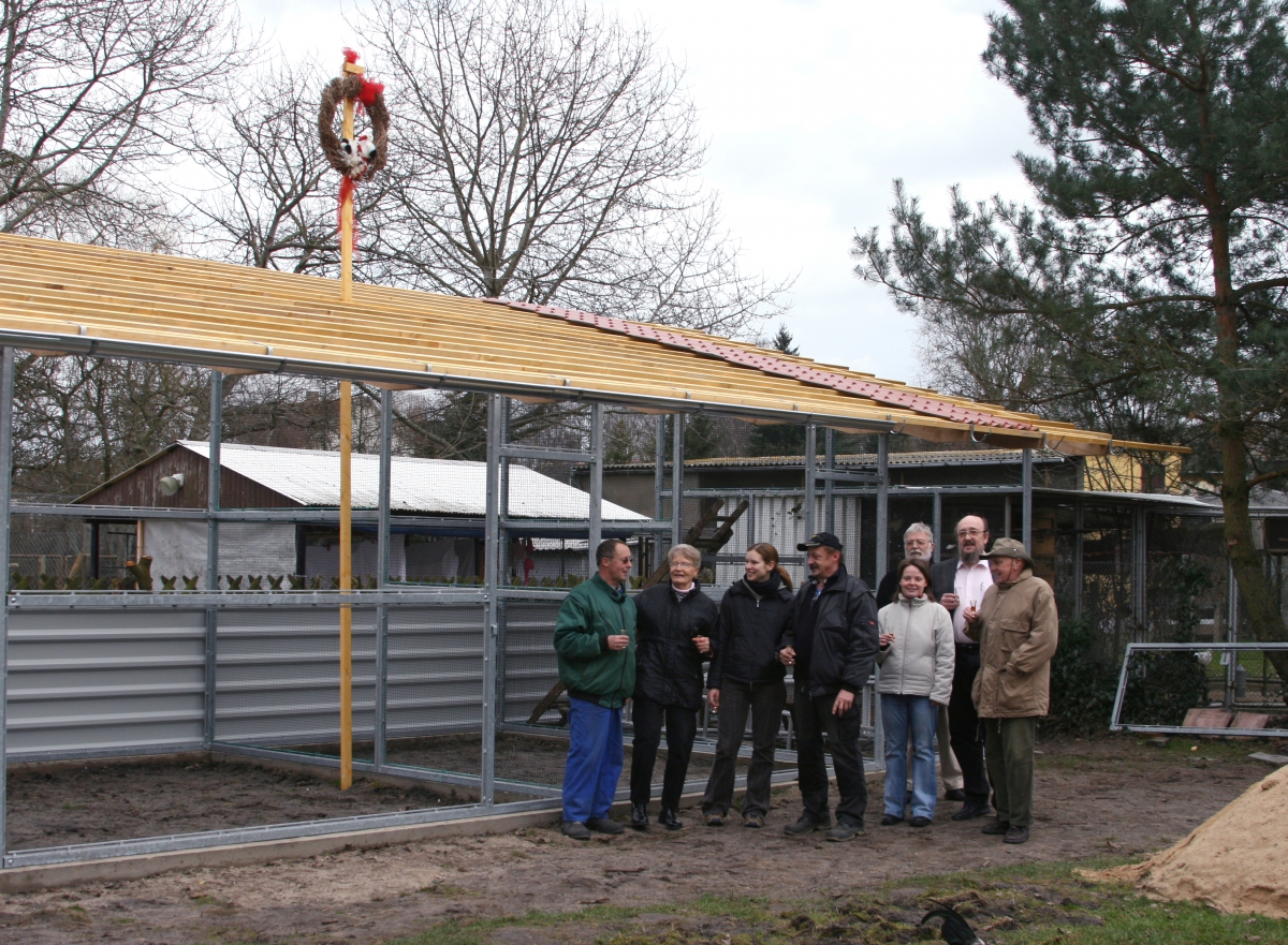 Personengruppe vor Rohbau eines Hauses mit Richtkranz